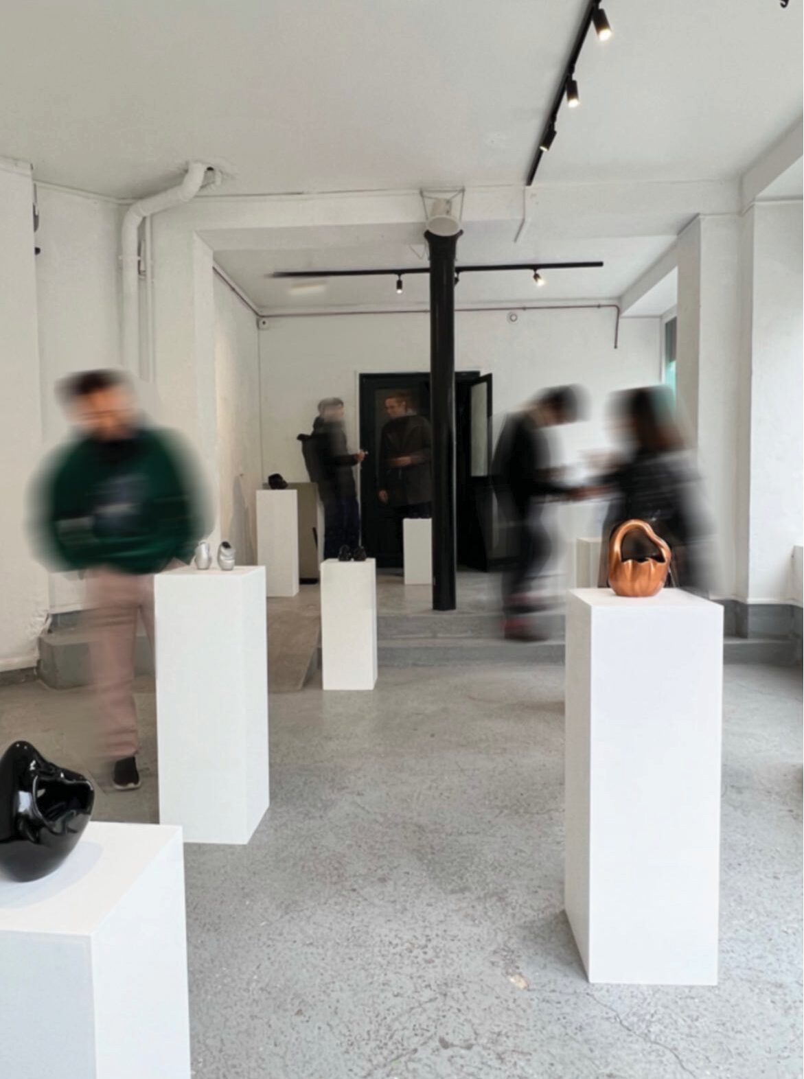 objects on white plinths in a gallery, visitors passing