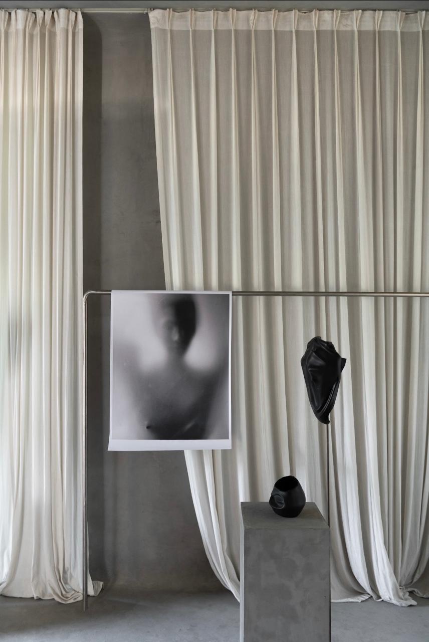 a print hung on a steel rail before silk curtains, with two black pieces
