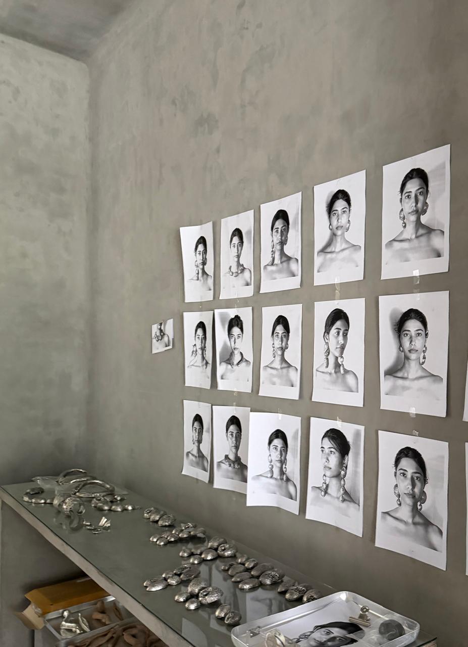 portrait prints pinned to the concrete wall over a table of silver pieces